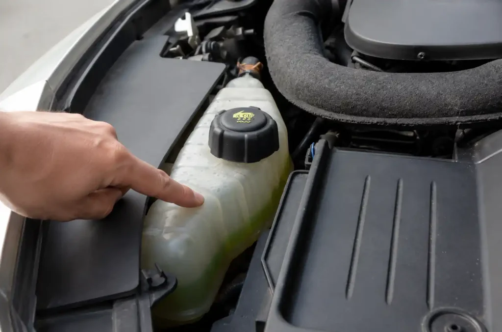 Main vérifiant le niveau de liquide de refroidissement sous le capot d’une Clio 3