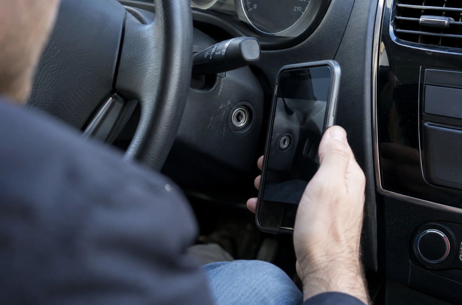 Automobiliste tenant un téléphone devant le contacteur de démarrage de sa voiture